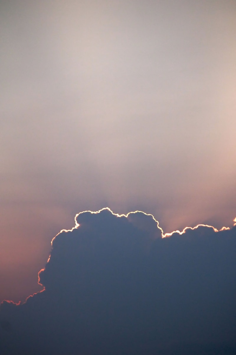 a plane flying through a cloudy sky at sunset